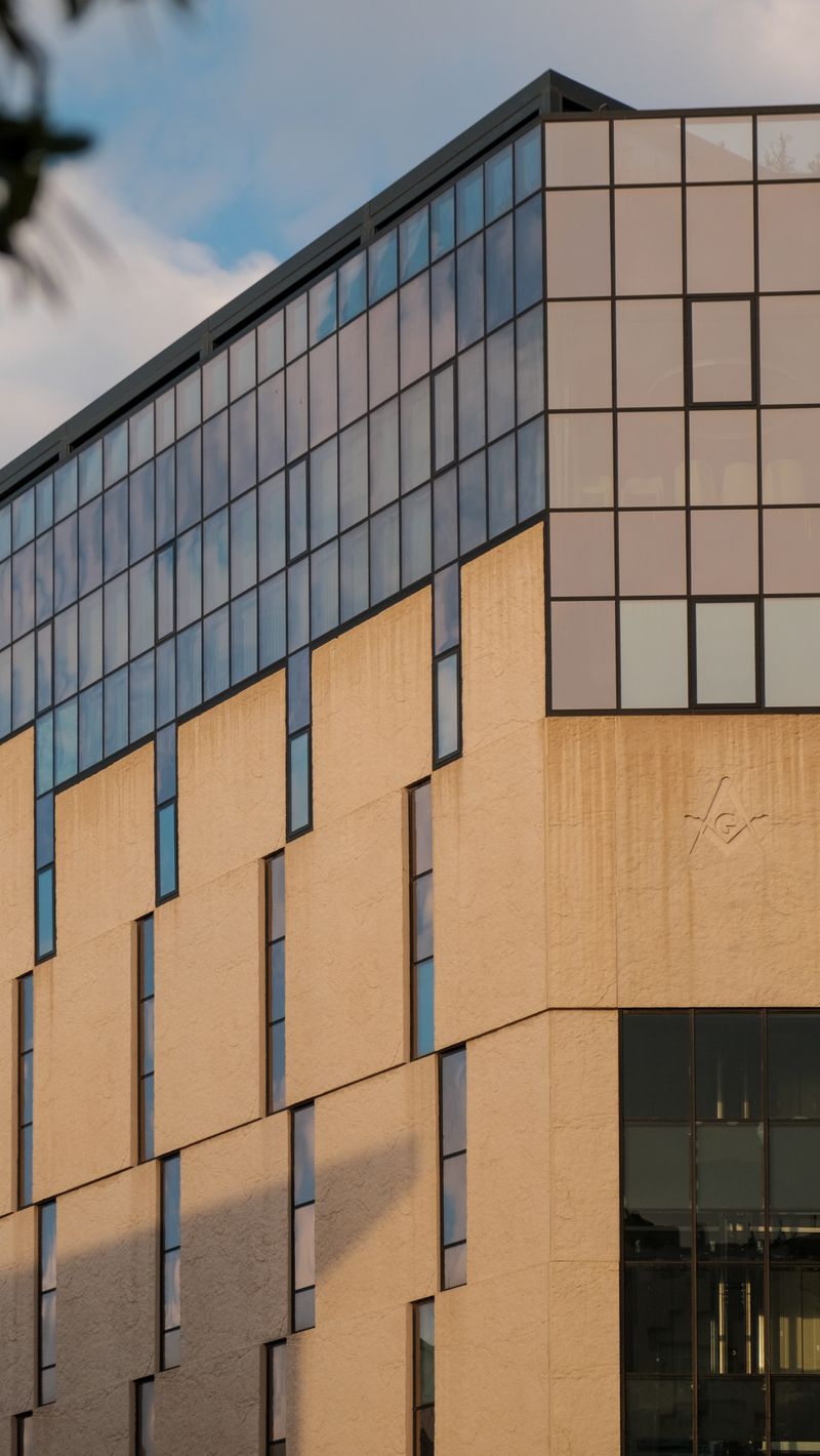 Fachada de um edifício corporativo moderno de vidro e pedra sob a luz dourada do fim de tarde.