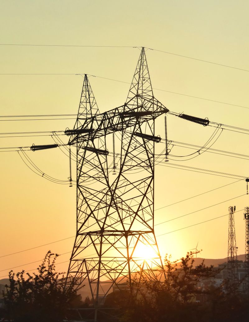 Torres de transmissão de energia elétrica de alta tensão recortadas contra o céu dourado do entardecer.